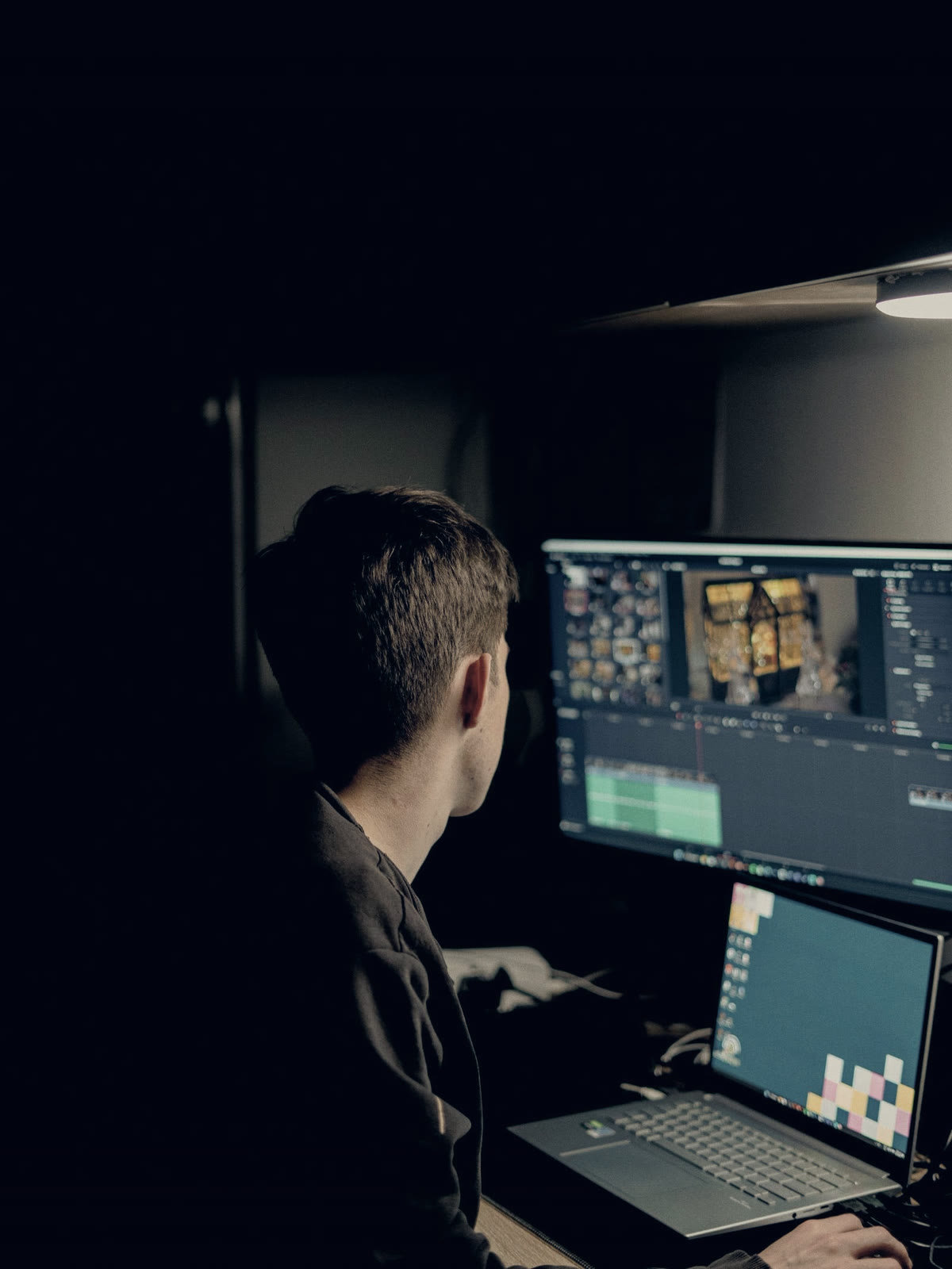A person editing a video on a laptop and a second monitor in a dark room