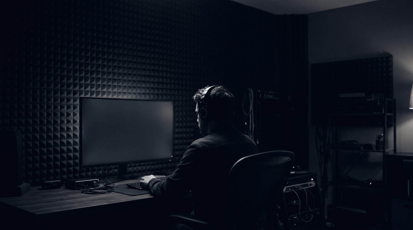 An editor in headphones working at a monitor in a dark, sound-treated edit room